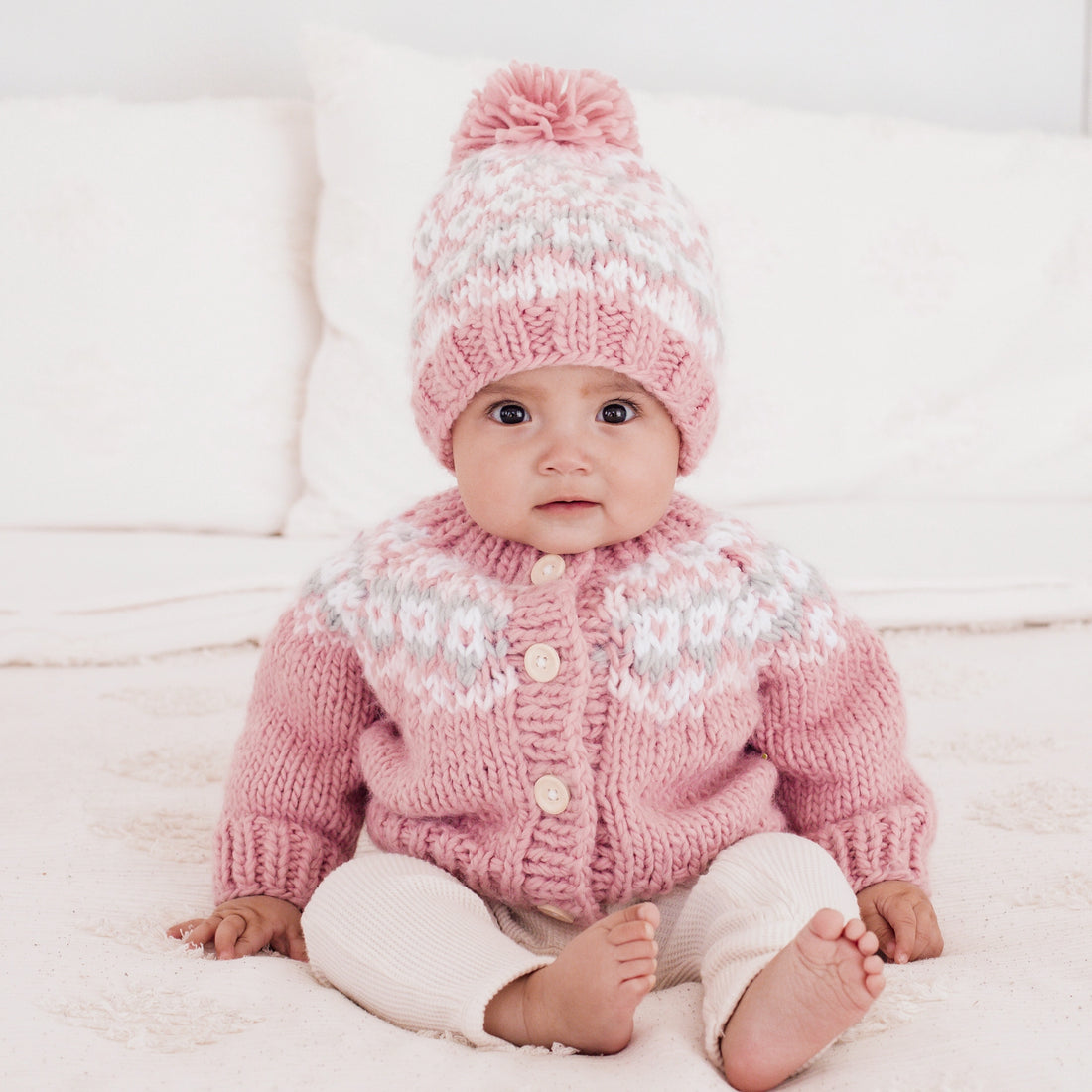 Baby wearing a pink knitted sweater and hat on a white background