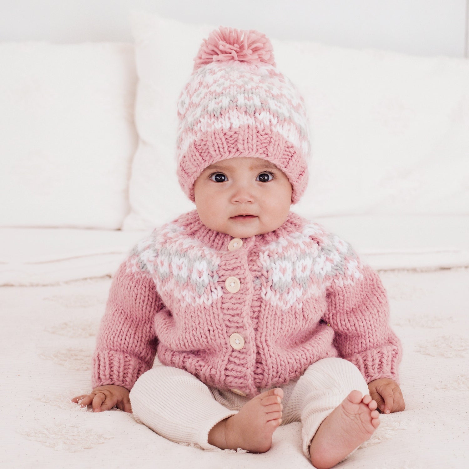 Baby wearing a pink knitted sweater and hat on a white background