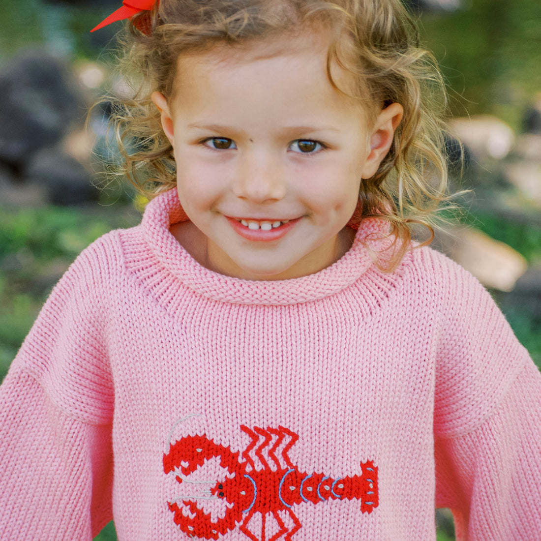 Young girl wearing a pink sweater with a red lobster design outdoors