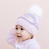 Baby wearing a pink knitted hat and scarf on a light beige background