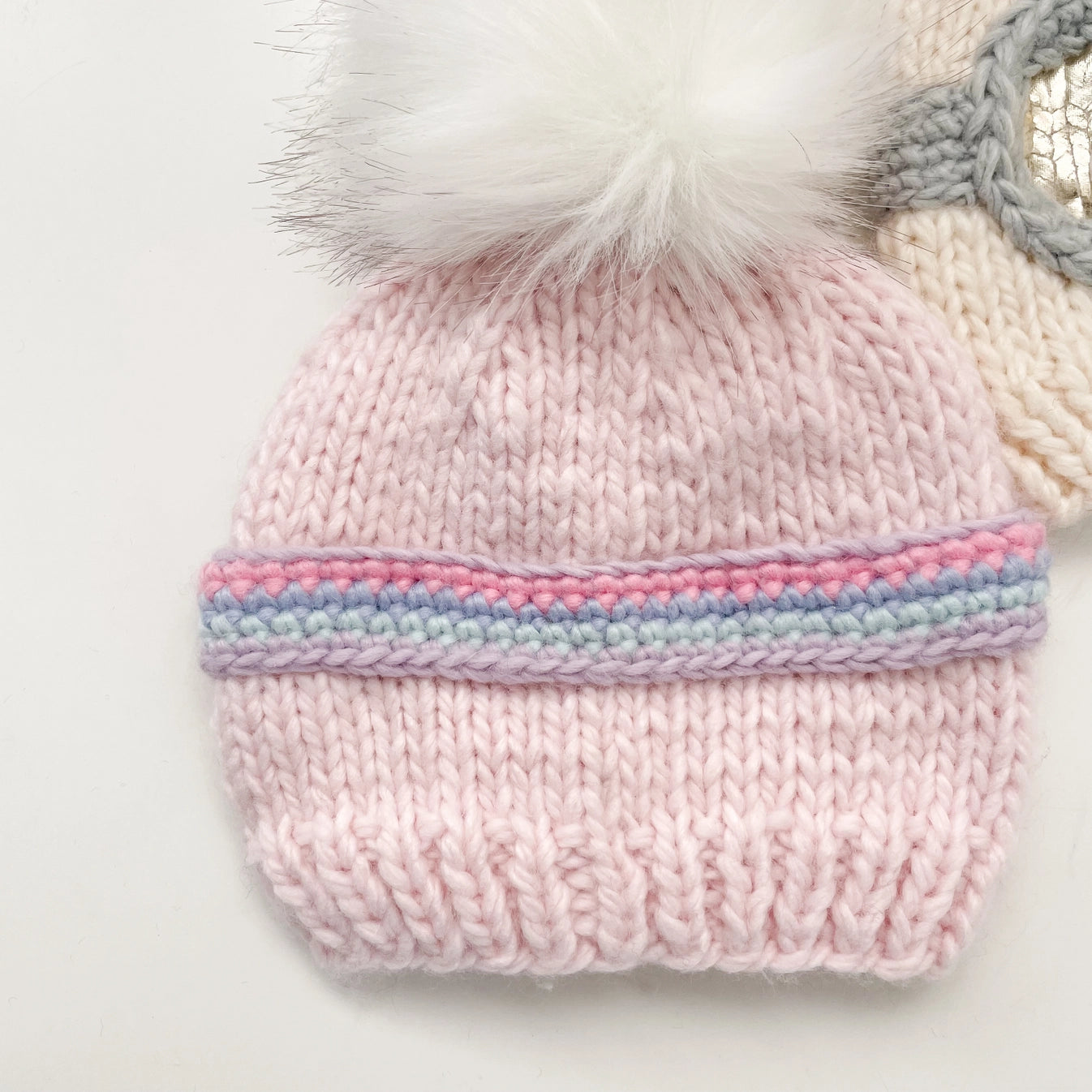 Pink knitted beanie with a colorful band and fur pom-pom on a light background
