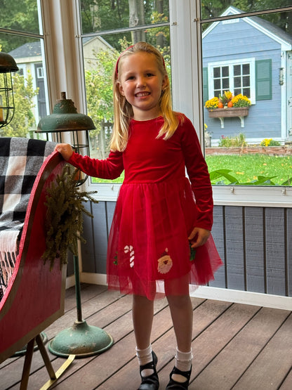 Young girl in a red dress standing on a wooden deck with a view of a house and garden.