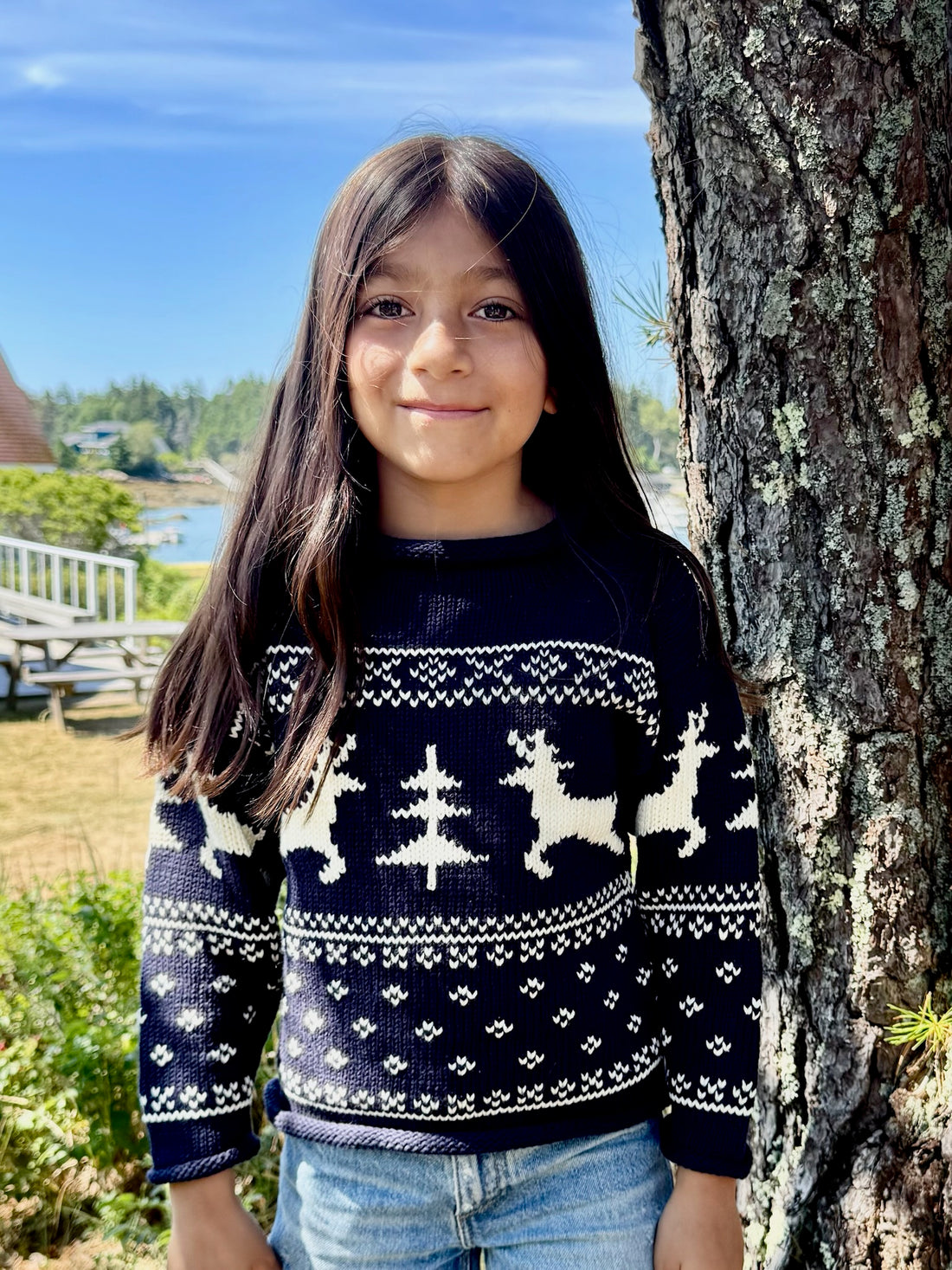 Child wearing a navy sweater with reindeer pattern standing next to a tree