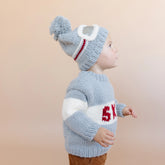 Child wearing a gray knit sweater and hat with a pom-pom on a beige background