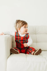 Child wearing a red plaid outfit sitting on a white couch.