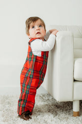 Child wearing red plaid pants and a white shirt standing on a white carpet next to a white couch.