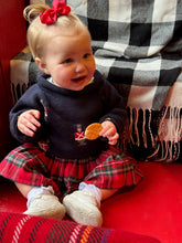 Child wearing a dark sweater with a red plaid skirt, sitting on a checkered surface.