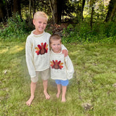 Two children wearing sweaters with turkey designs standing in a grassy area.