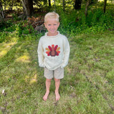 Young boy wearing a sweater with a turkey design outdoors in a grassy area.