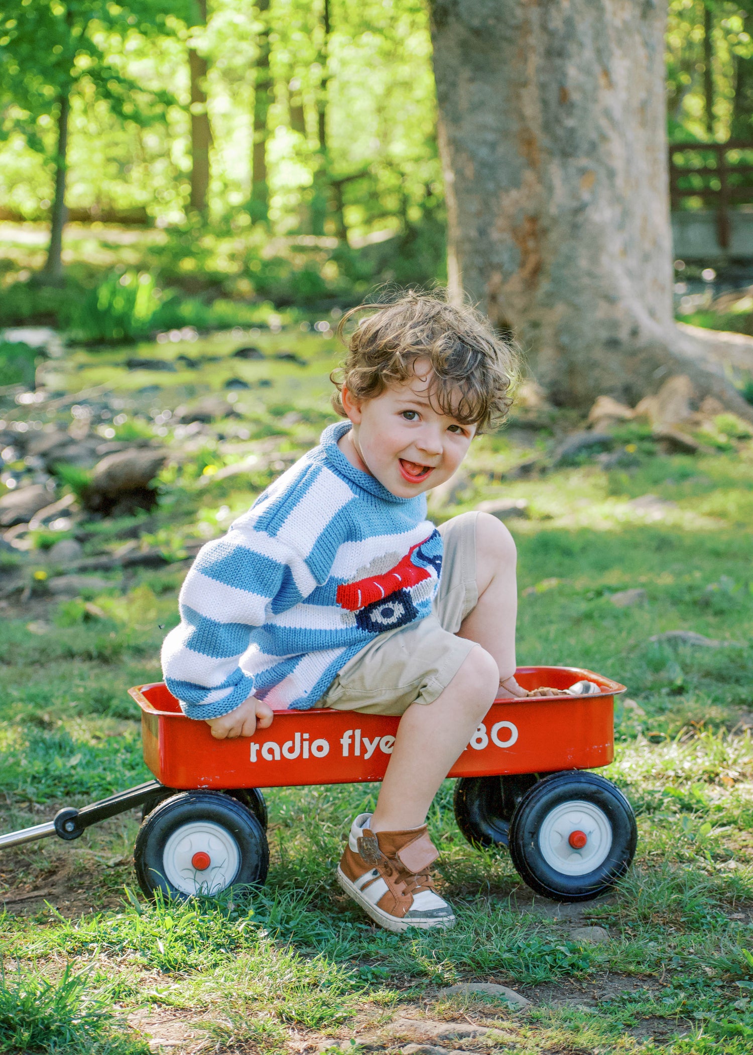 boy in red wagon wearing blue striped dump truck sweater