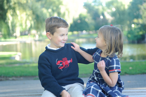 boy wearing Navy Lobster Roll Neck Sweater sitting with girl in navy dress with hands on each other's shoulders