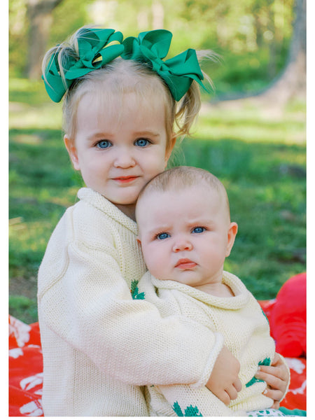big sister and little sister wearing sweaters and green hair bows