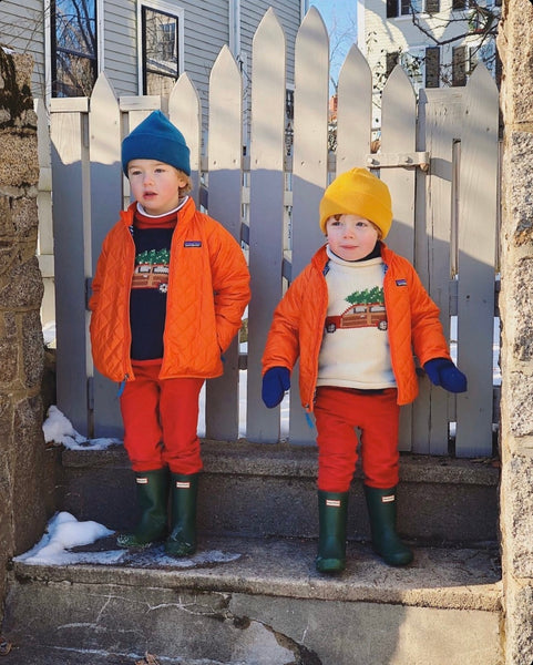 two children wearing sweaters with orange jackets over