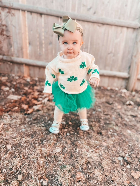 baby girl wearing ivory shamrock roll neck sweater paired with green tutu, sneakers and gold hair bow