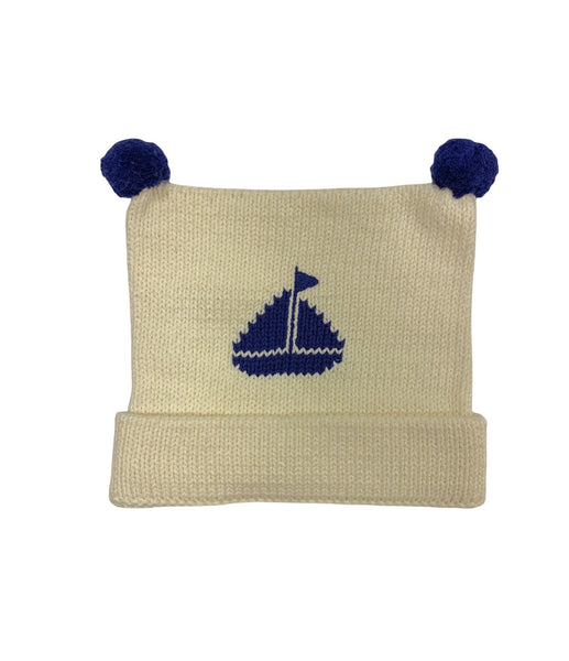 ivory hat, bottom is rolled up once with blue poms at top and blue sailboat knitted in center