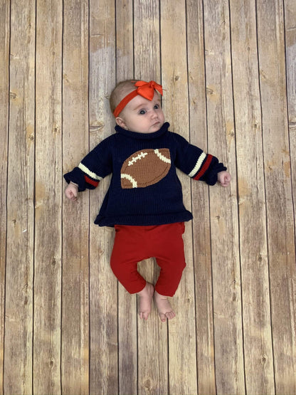 baby girl wearing Navy Football Roll Neck Sweater paired with red leggings and a red hair bow