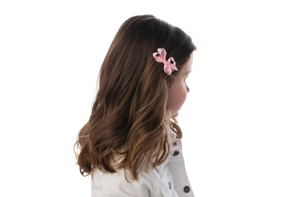 girl with light brown hair wearing the extra small size bow in light pink in her hair