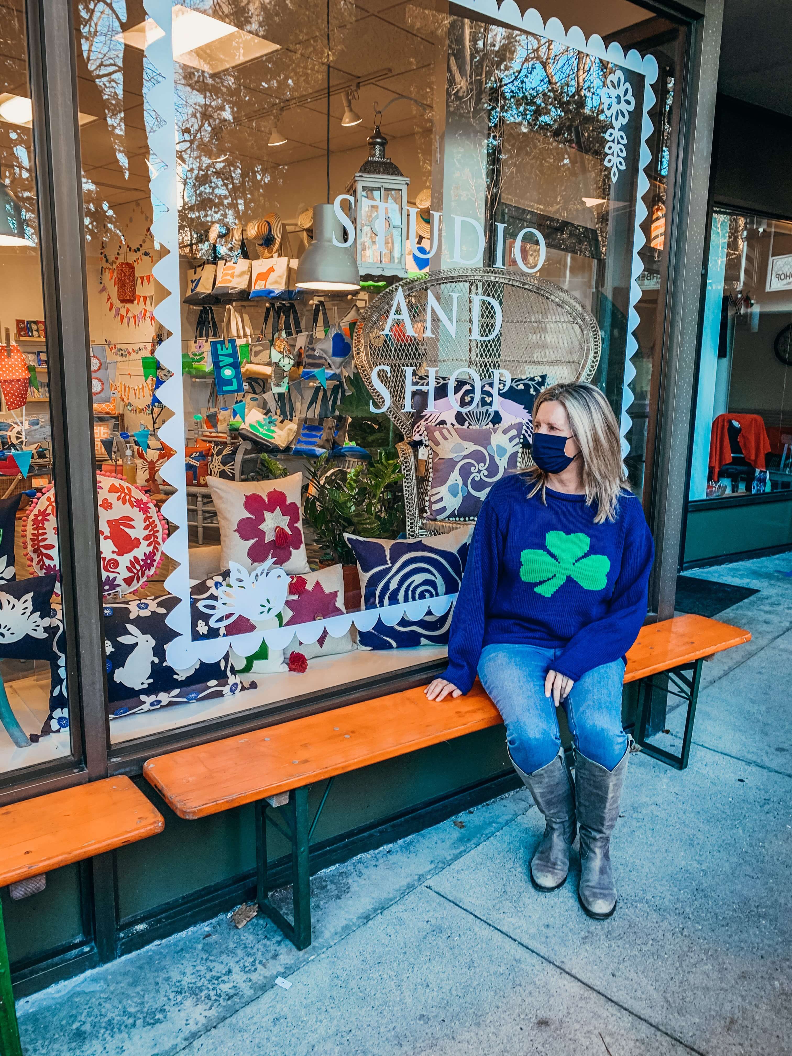 woman sitting on a bench wearing the Ladies Navy Shamrock Sweater with jeans and boots
