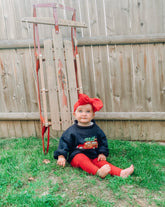 baby wearing navy woody wagon sweater by a sled